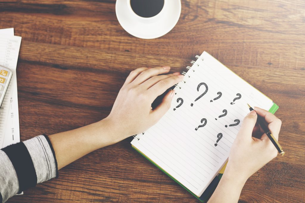 A pair of hands writing question marks on a notebook.