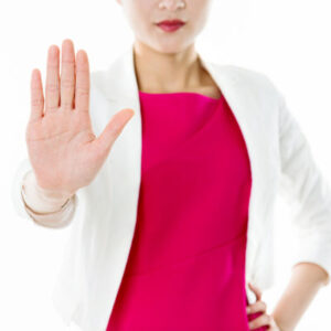 A woman in a red shirt and a white coat holding up her hand in a stop motion.