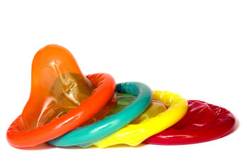 Four different colored condoms (orange, green, yellow, red) stacked next to each other.