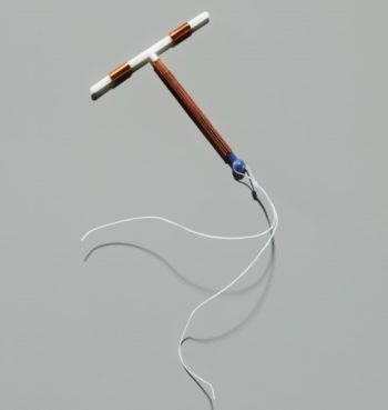 A T-shaped copper IUD with two white strings at the end