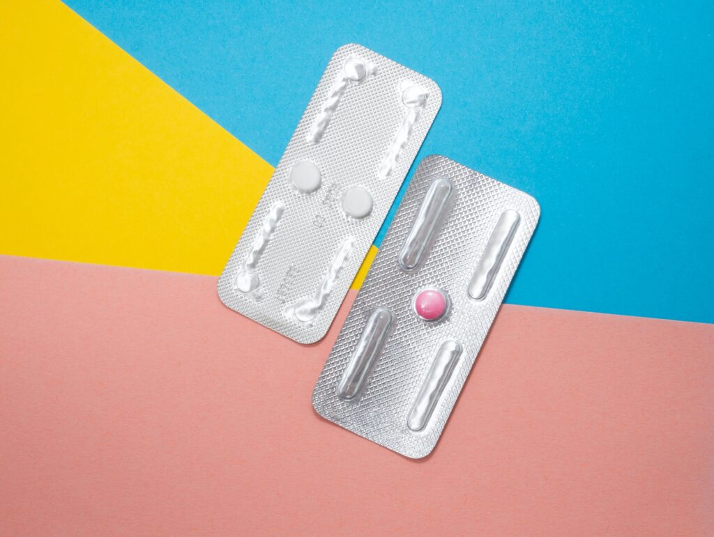 Two packages of pills, one with two white pills and one with a single pink pill. 
