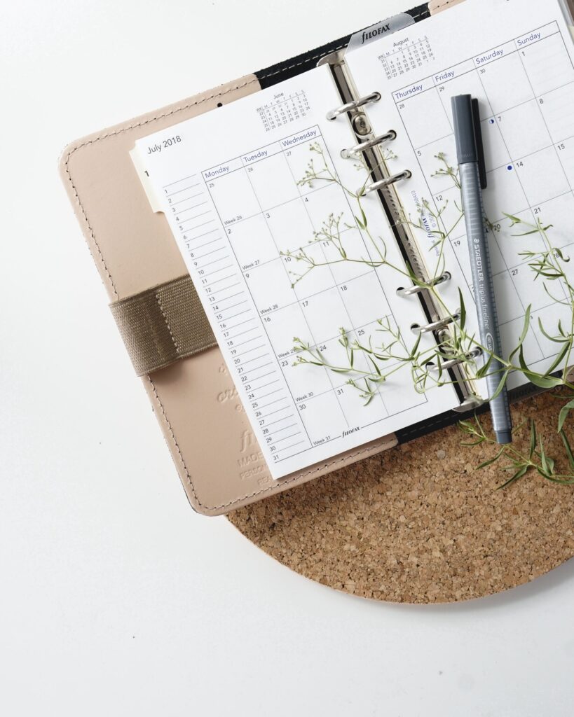 An open calendar notebook with a pen and a plant on it. 