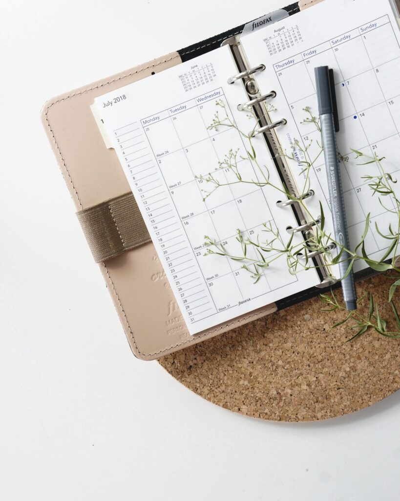 Un cuaderno de calendario abierto con un bolígrafo y una planta.