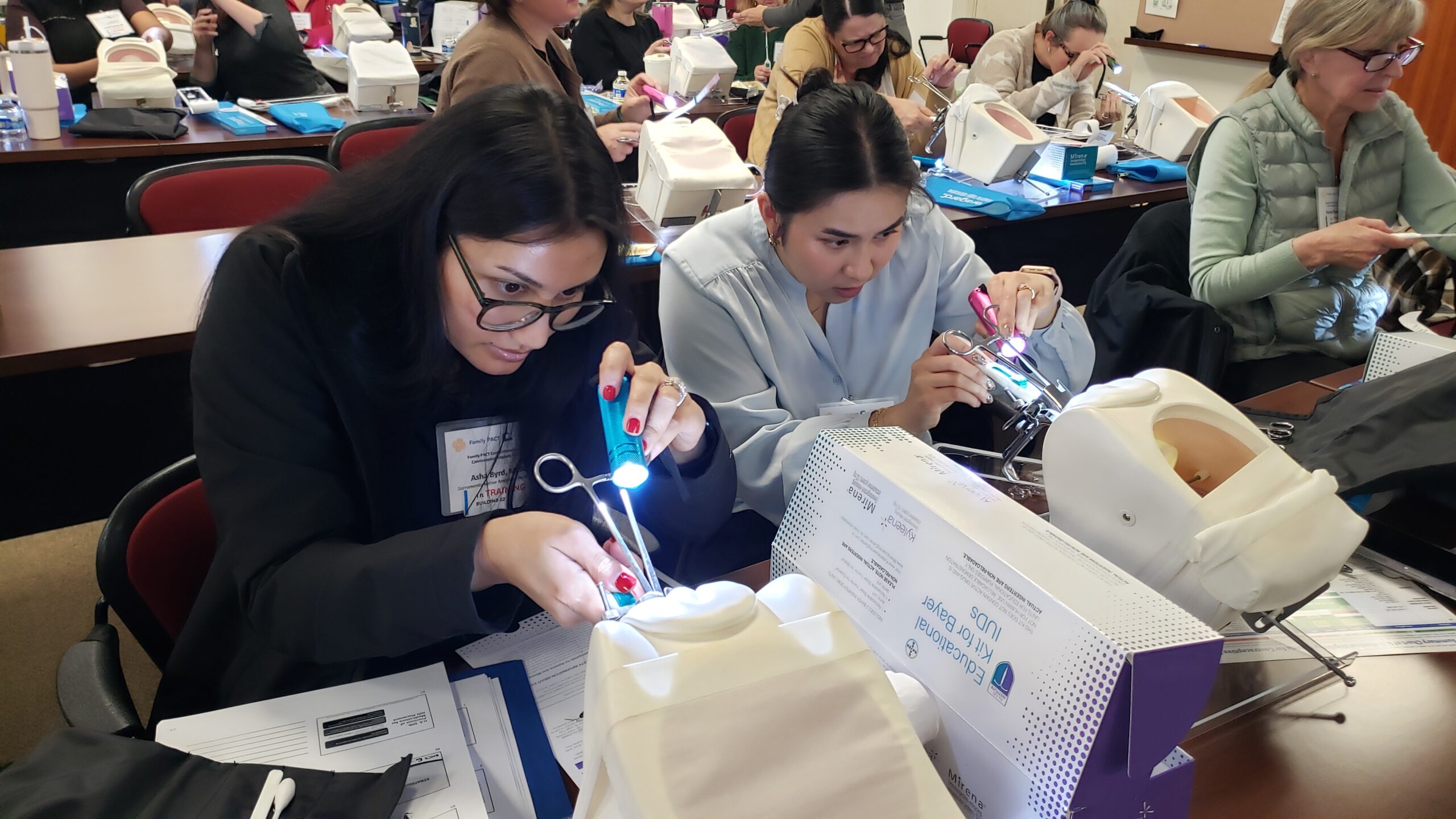Two female clinician practicing placing intrauterine devices (IUDs) on plastic pelvic models.
