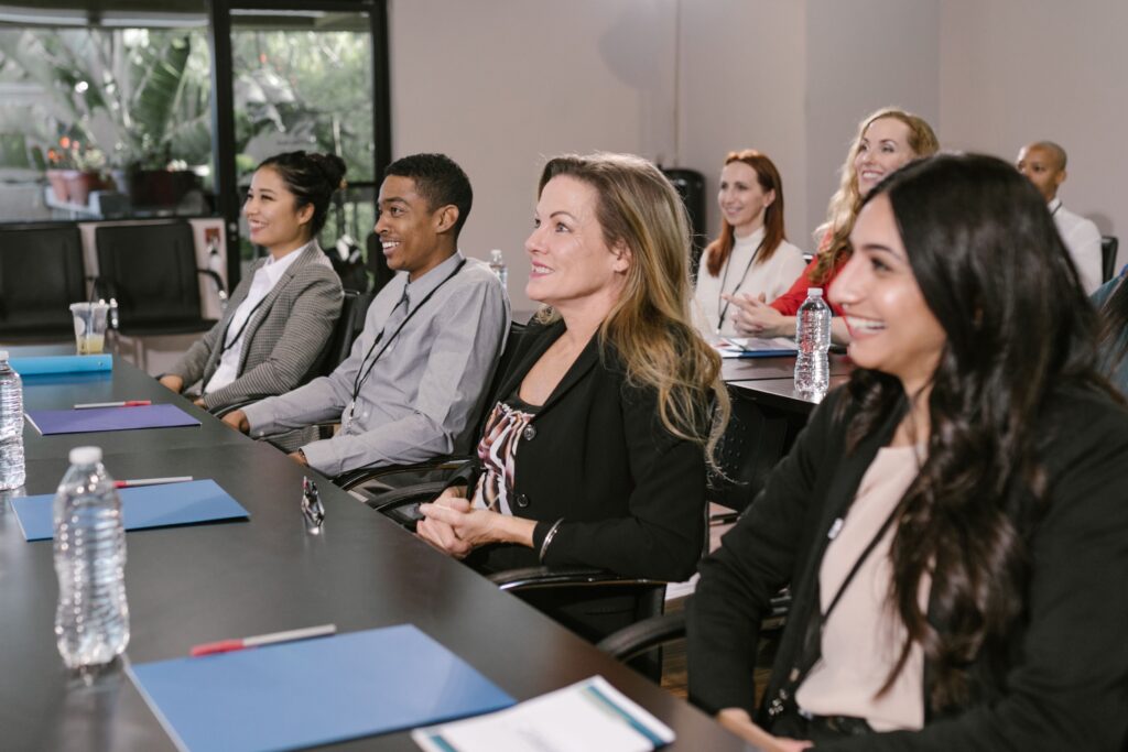A row of diverse people sitting at a long, black table in a training room.